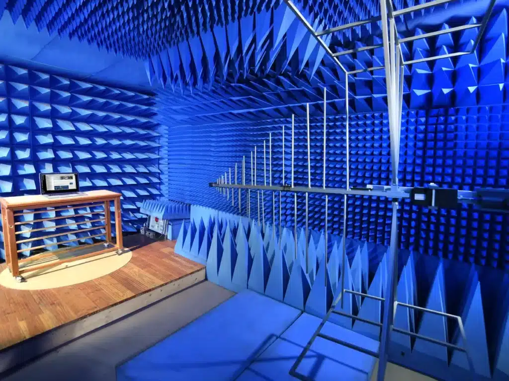 Equipo bajo ensayo sobre la mesa de madera de la cámara anecoica del laboratorio EMC de telproCE, con la antena logoperiódica de medida delante